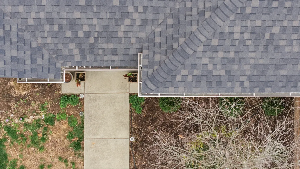 White gutters and downspouts along the edge of a shingle roof, seen from above
