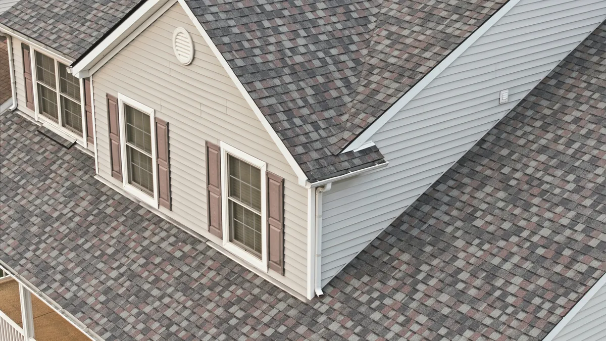 Cream siding with shutters beside a new multi tone shingle roof